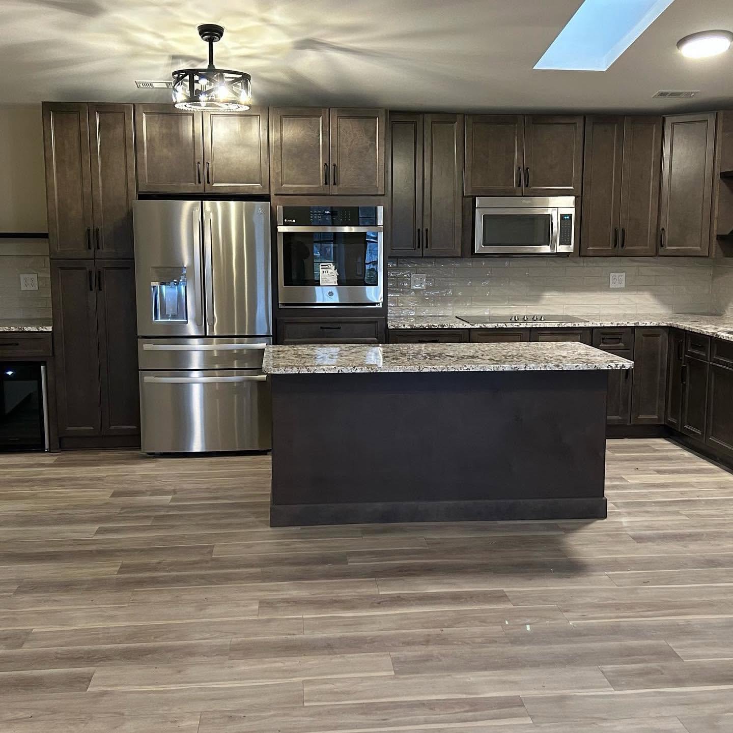 A finished kitchen: dark shaker cabinets, stainless steel appliances, a granite-topped island and wood-look plank flooring.
