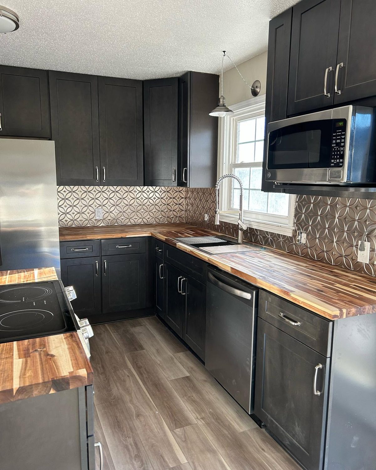 The kitchen at 1711 Colby: dark brown shaker cabinets, butcher-block worktops, a patterned cream and grey tiled backsplash, stainless steel appliances and grey wood-look plank flooring.