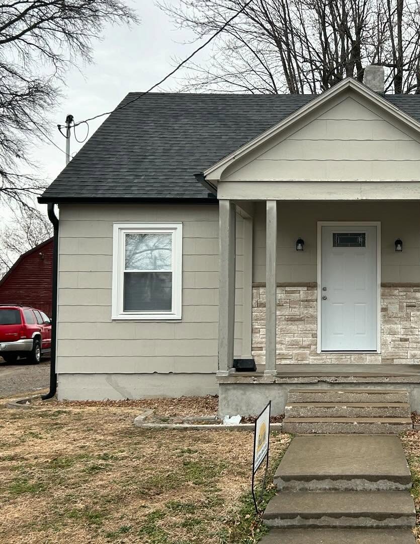 677 Clay as posted in March 2025: a single-storey house with beige lap siding, a stone-faced porch base under a gabled porch on square columns, a white front door, a window with white trim and a dark shingled roof.